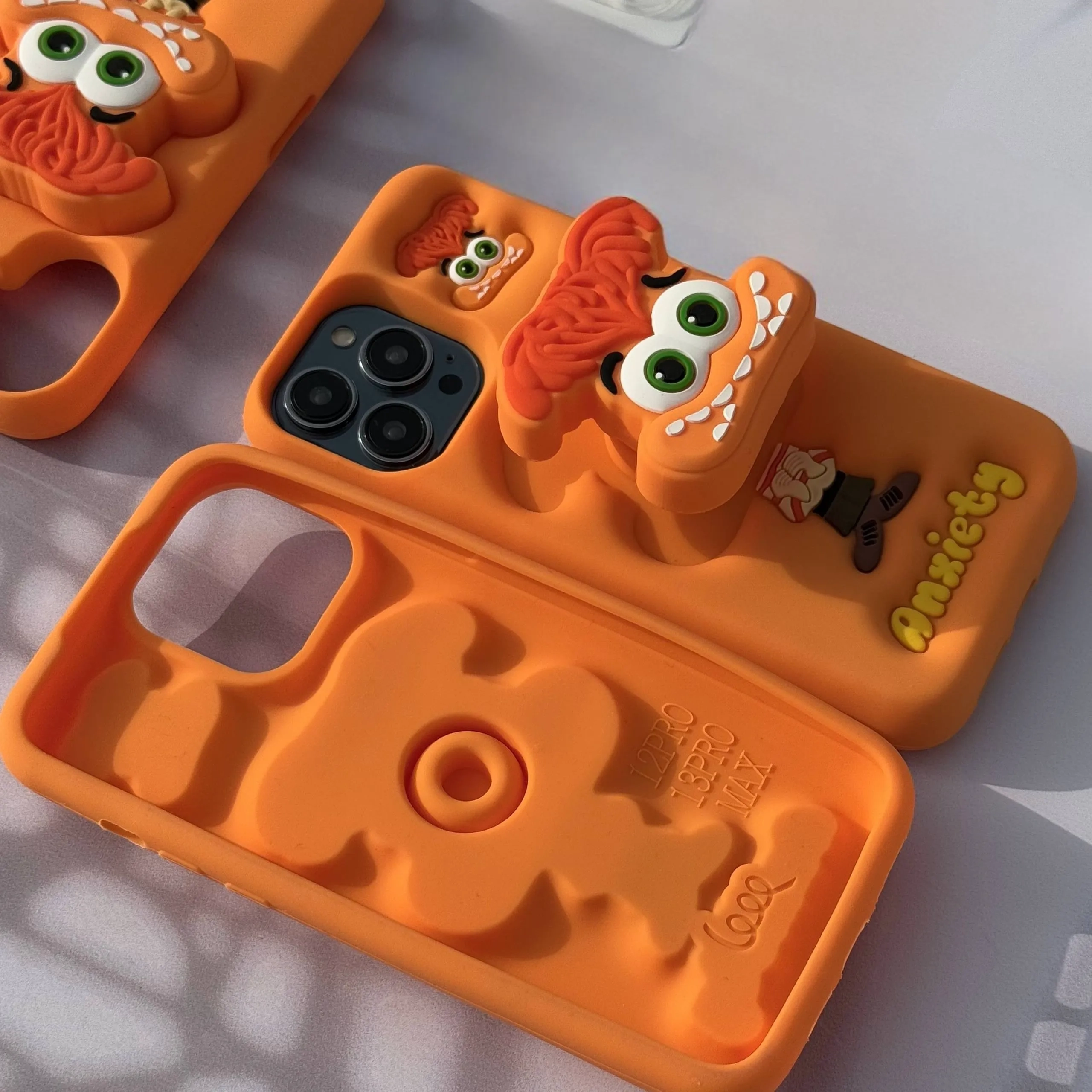 قاب گوشی آیفون سیلیکونی نارنجی طرح عروسکی شخصیت اضطراب با استند قاب گوشی آیفون سیلیکونی نارنجی طرح عروسکی شخصیت اضطراب با استند